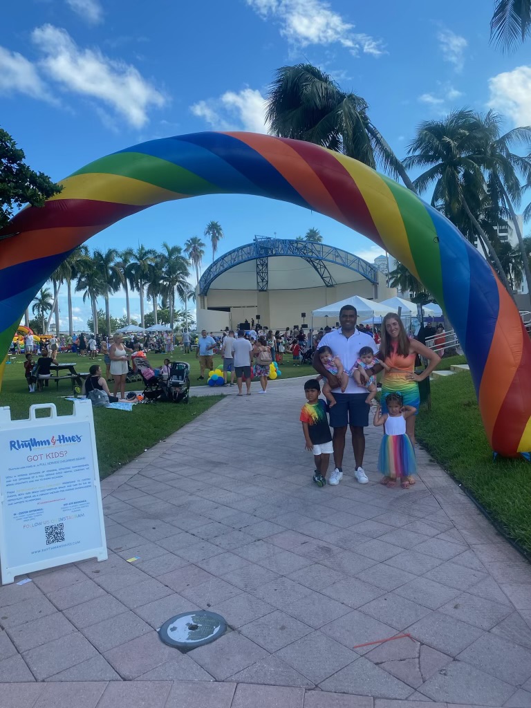 A family walking under a giant rainbow arch at a community festival