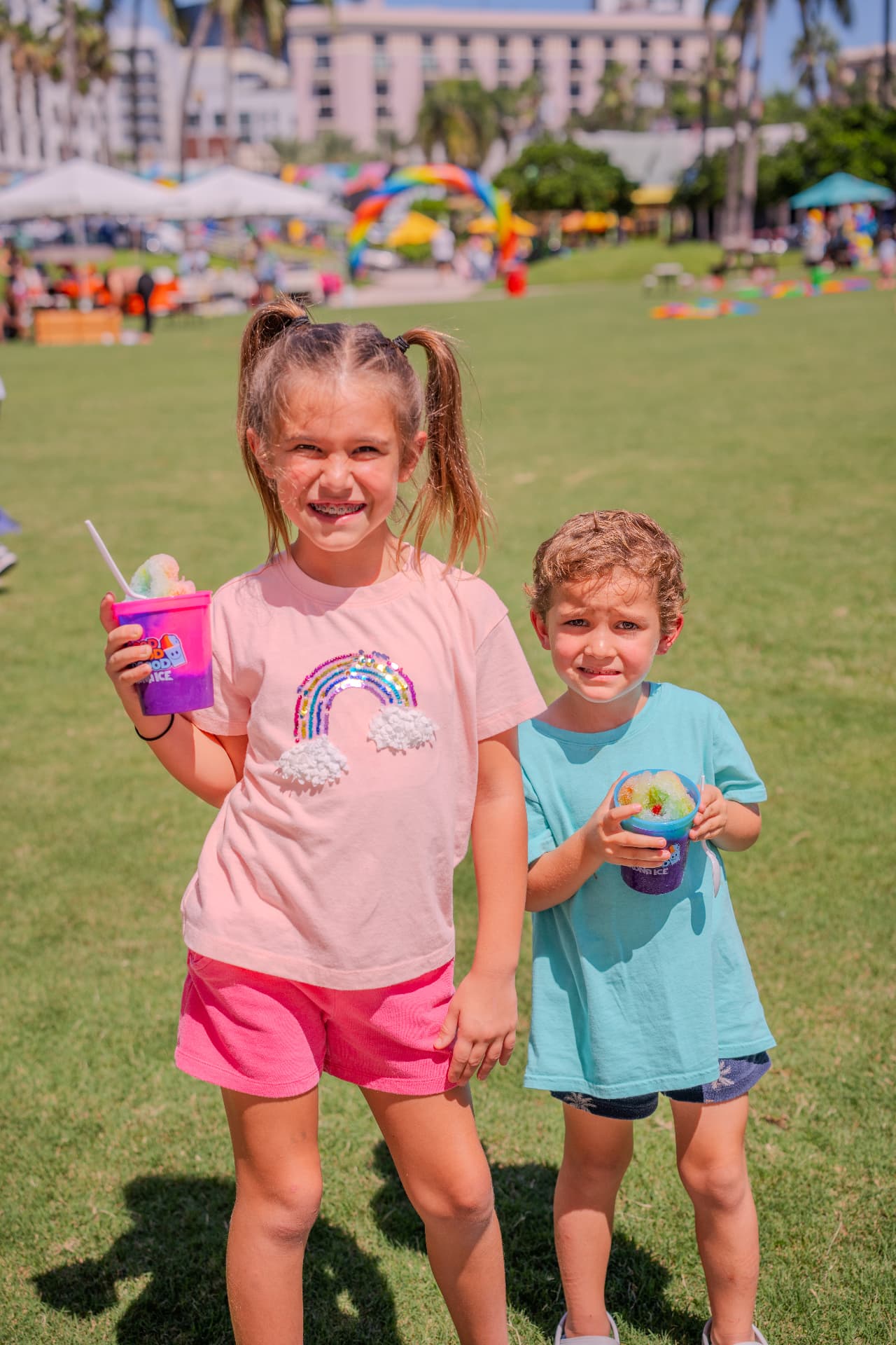 Two children smiling with rainbow snow cones at a community festival